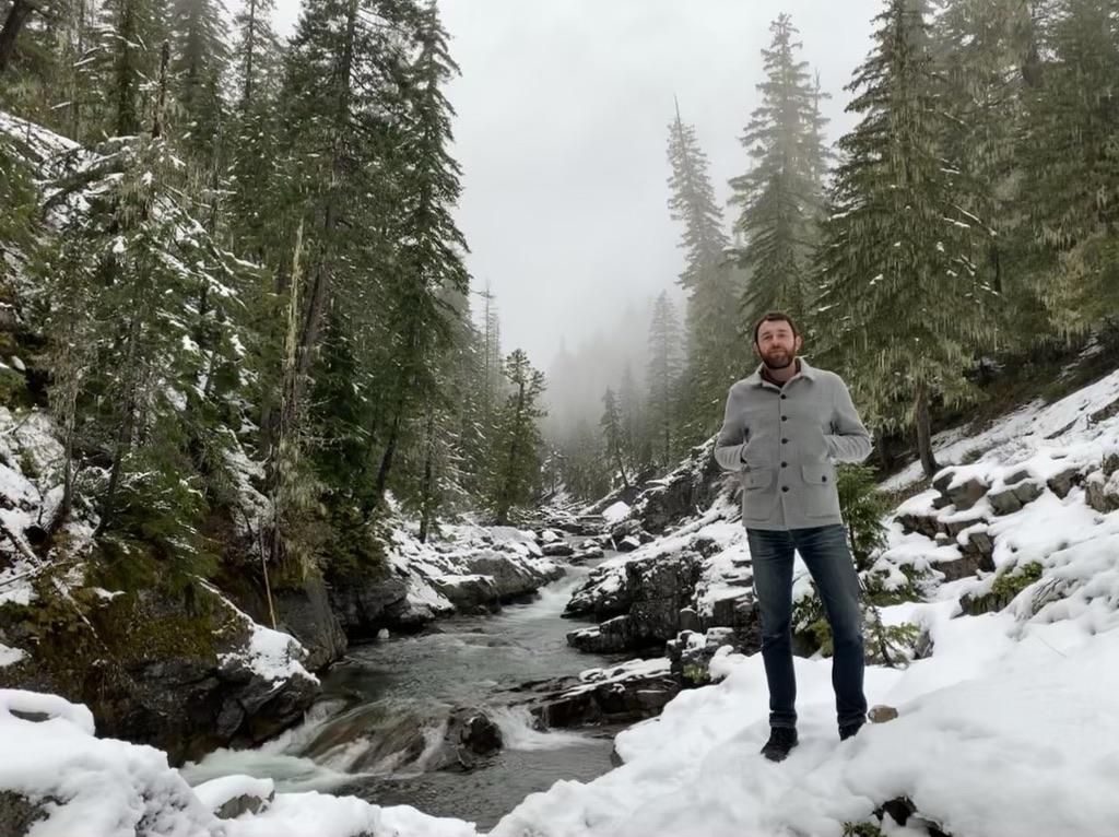 Leon beside a stream in a snowy evergreen forest